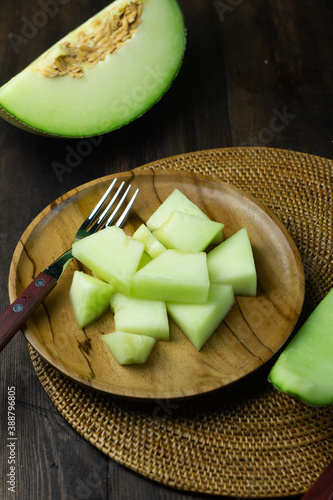Buah Melon or Fresh melon fruit served on wooden brown plate with a fork. Dark wooden background.