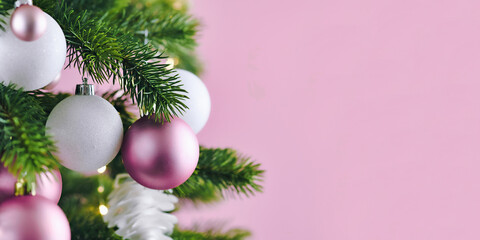 Banner with Christmas tree decorated with white and pink seasonal tree ornament baubles on pink background with empty copy space
