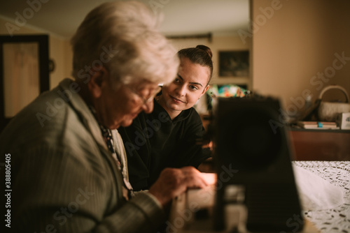 A senior caucasian grandmother teaches her smiling teenage granddaughter to sew on a sewing machine. Grandma's education