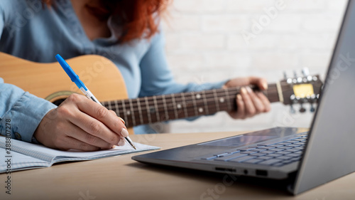 Fotografi A woman with a guitar writes notes in a notebook