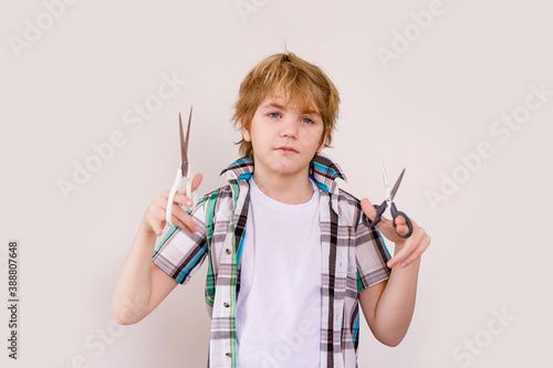 Happy blonde boy European appearance in a white shirt holding scissors on a white background