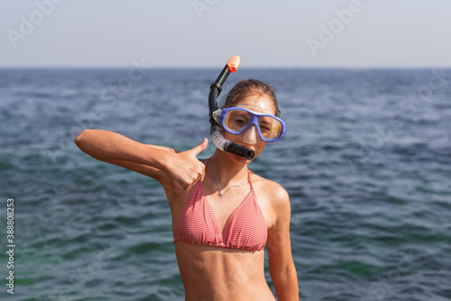Happy baby girl in mask and snorkel on the beach in summer with sea background
