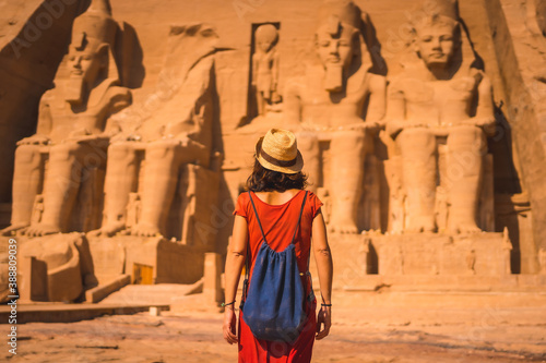 A young tourist in a red dress and straw hat walking towards the Abu Simbel Temple in southern Egypt in Nubia next to Lake Nasser. Temple of Pharaoh Ramses II, travel lifestyle