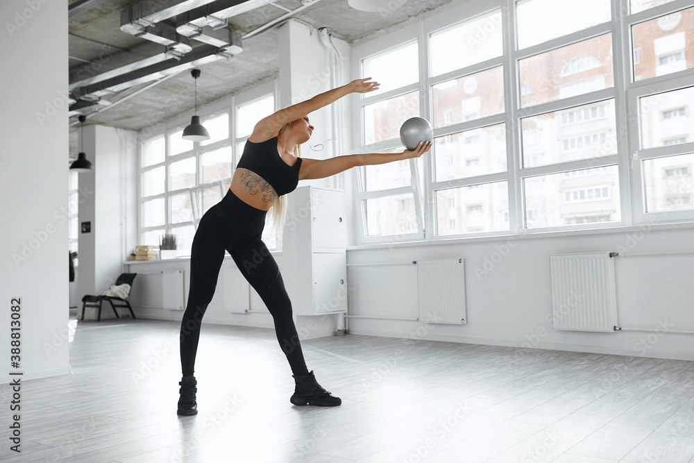 blonde warms up in the gym. A young sportswoman in a black suit gives a stretching while standing in the trunk hall. gymnastics blonde warms up in the gym. A young sportswoman in a black suit gives a stretching while standing in the trunk hall. gymnastics