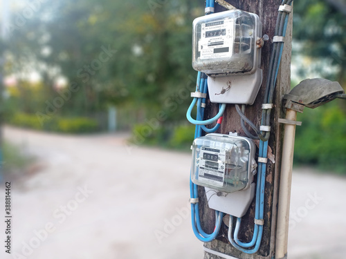 Chiangrai,Thailand, October 2020: 2 electric meters power with the pole next to street in a countryside village isolated on blurred background.