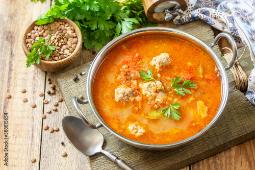 Tomato lentil soup with meatballs and vegetables on a wooden table.