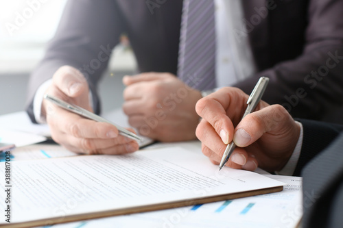 Male arm in suit and tie fill form clipped pad with silver pen closeup. Sign gesture read pact sale agent bank job make note loan credit mortgage investment finance executive chief legal teamwork law