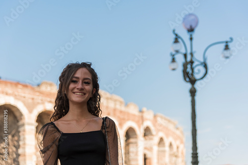 Half-length portrait of young girl with curly brown hair smiling outdoors. In the background of the city, arena of Verona, Italy. © Roza_Sean