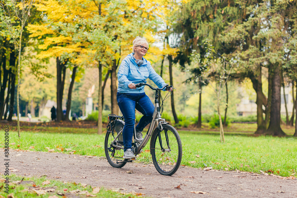 senior woman walking in the park with a bicycle, sunny day