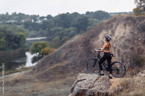 Fit young woman wearing sportswear standing with her bicycle on rocky background