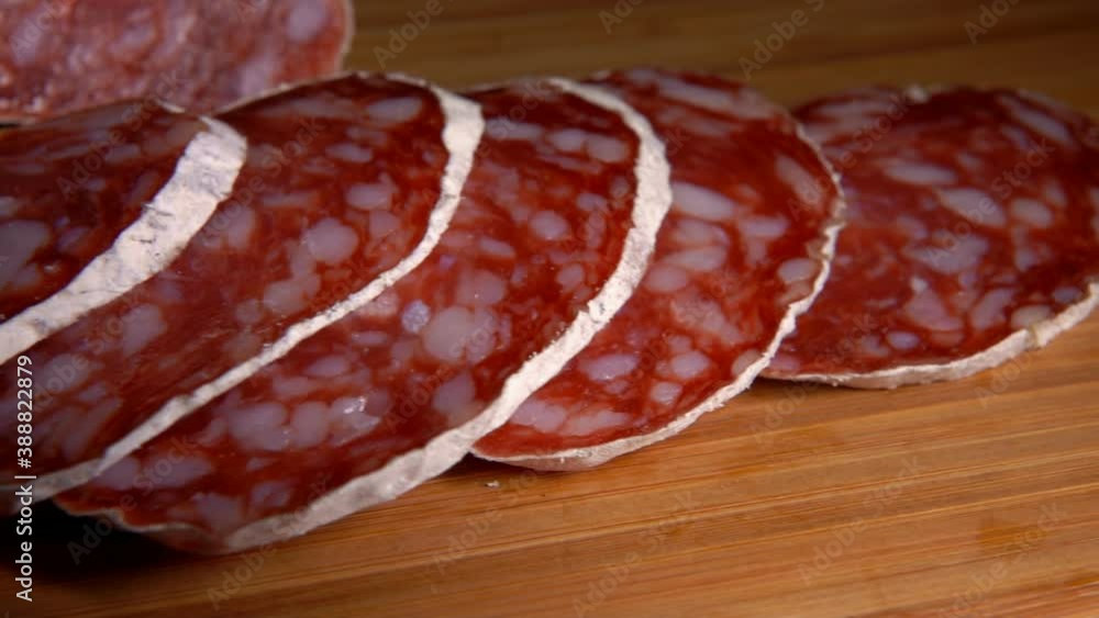 Close-up panorama of delicious dry sausage taken from a wooden board with a fork on the background of pepper and greenery Close-up panorama of delicious dry sausage taken from a wooden board with a fork on the background of pepper and greenery