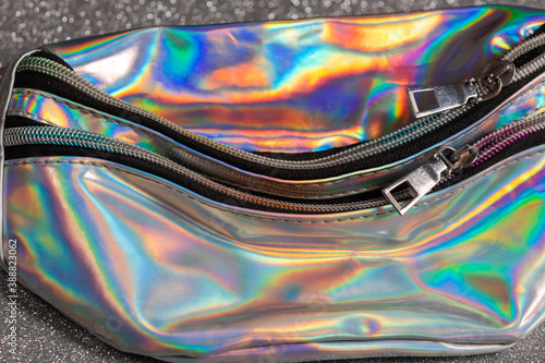Selected focus of Zipper on a neon holographic color bag on the bokeh silver background.