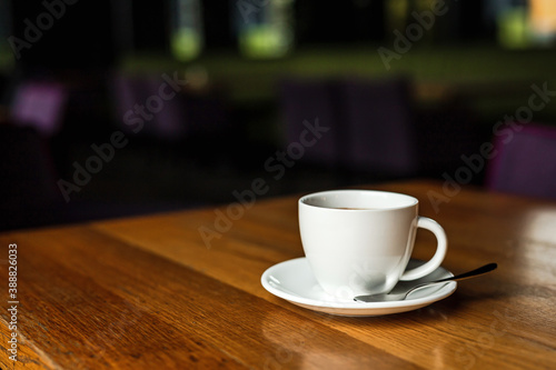 A white cup of black coffee, white saucer, spoon, wooden table, at a cafe