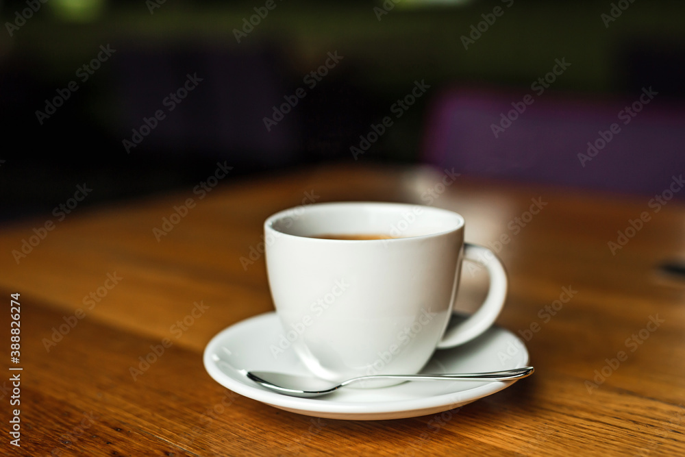 A white cup of black coffee, white saucer, spoon, wooden table, at a cafe A white cup of black coffee, white saucer, spoon, wooden table, at a cafe
