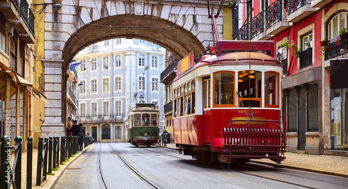Lisbon, Portugal. Vintage red retro tram on narrow bystreet tramline in Alfama district of old town. Popular touristic attraction of Lisboa city. Public tramways trasport. photo