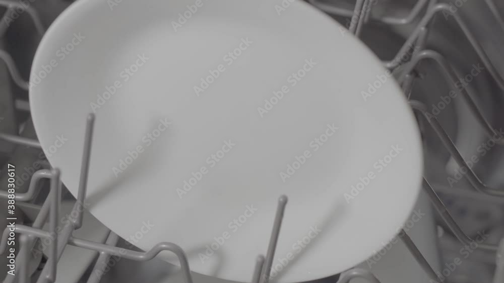 White plate being placed and removed from the top rack of a modern residential dishwasher. White plate being placed and removed from the top rack of a modern residential dishwasher.