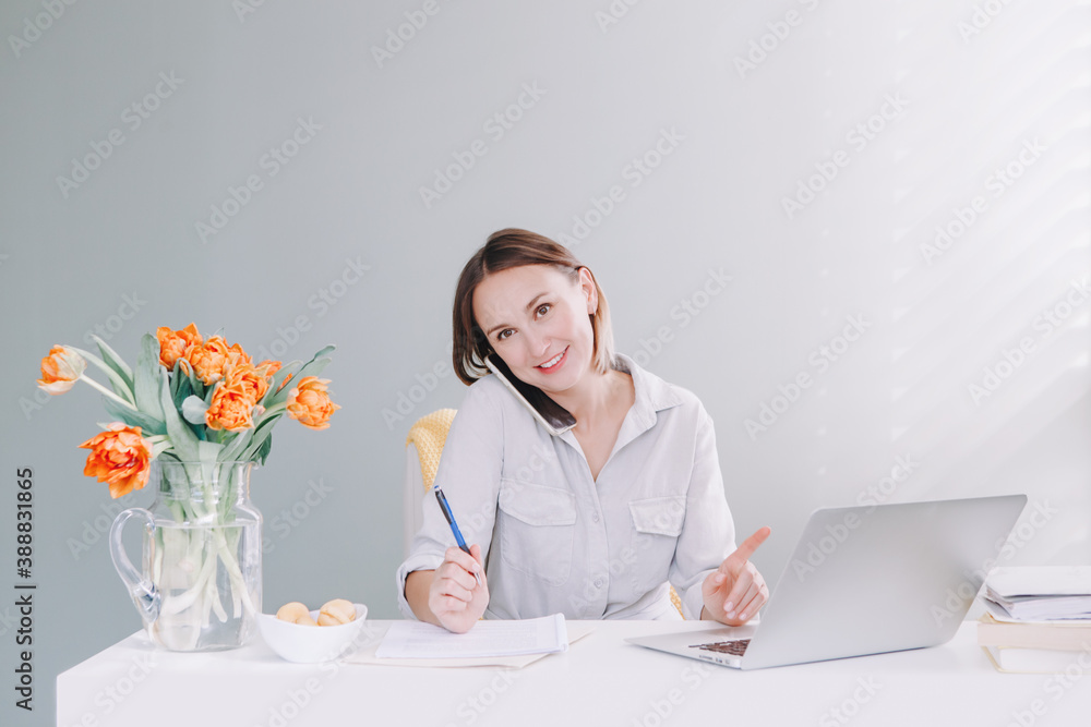 Beautiful middle age woman at desktop table working on laptop computer. Work business from home. Remote distant studying and working. Young woman talking on mobile phone. Beautiful middle age woman at desktop table working on laptop computer. Work business from home. Remote distant studying and working. Young woman talking on mobile phone.