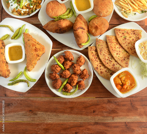 Assorted Indian Tea time snacks in group includes Spicy onion fritters, bread pakora,samosa, kachori and aloo paratha on wooden background. Dishes and appetizers of indian cuisine