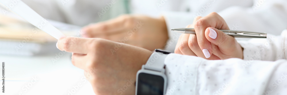Focus on female arm in watches. Smart businesswoman holding metallic writing pen and sitting with friendly colleague discussing something important. Accounting office concept. Blurred background