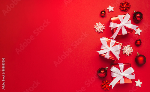 Merry Christmas and Happy Holidays greeting card background with copyspace on the left. Red Christmas gifts decor on red background top view. Winter xmas holiday theme in flat lay