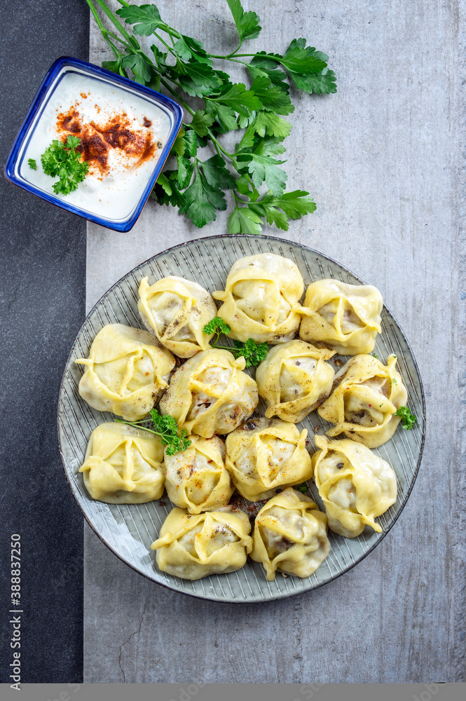 Traditional steamed Russian pelmeni with yoghurt cayenne pepper offered as top view on a rustic design plate Traditional steamed Russian pelmeni with yoghurt cayenne pepper offered as top view on a rustic design plate
