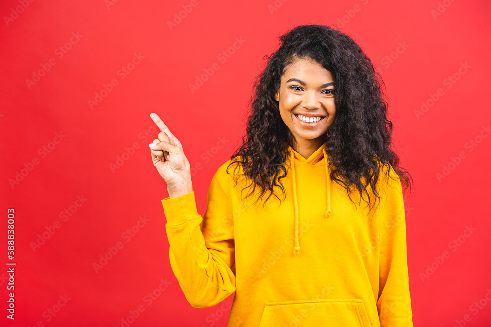 Portrait of a happy young african american curly woman pointing fingers up at copy space isolated over red background. Portrait of a happy young african american curly woman pointing fingers up at copy space isolated over red background.