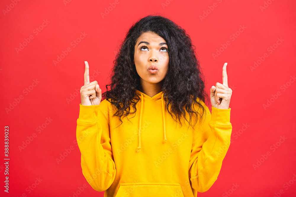 Portrait of a happy young african american curly woman pointing fingers up at copy space isolated over red background. Portrait of a happy young african american curly woman pointing fingers up at copy space isolated over red background.
