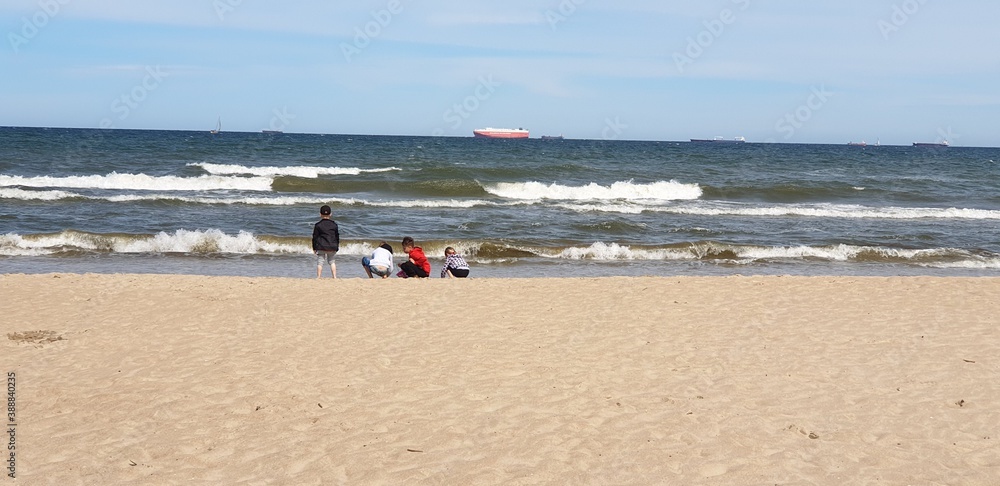 Czwórka dzieci nad brzegem morza odwrócona tyłem bawi sie w wodzie - obrazy, fototapety, plakaty 