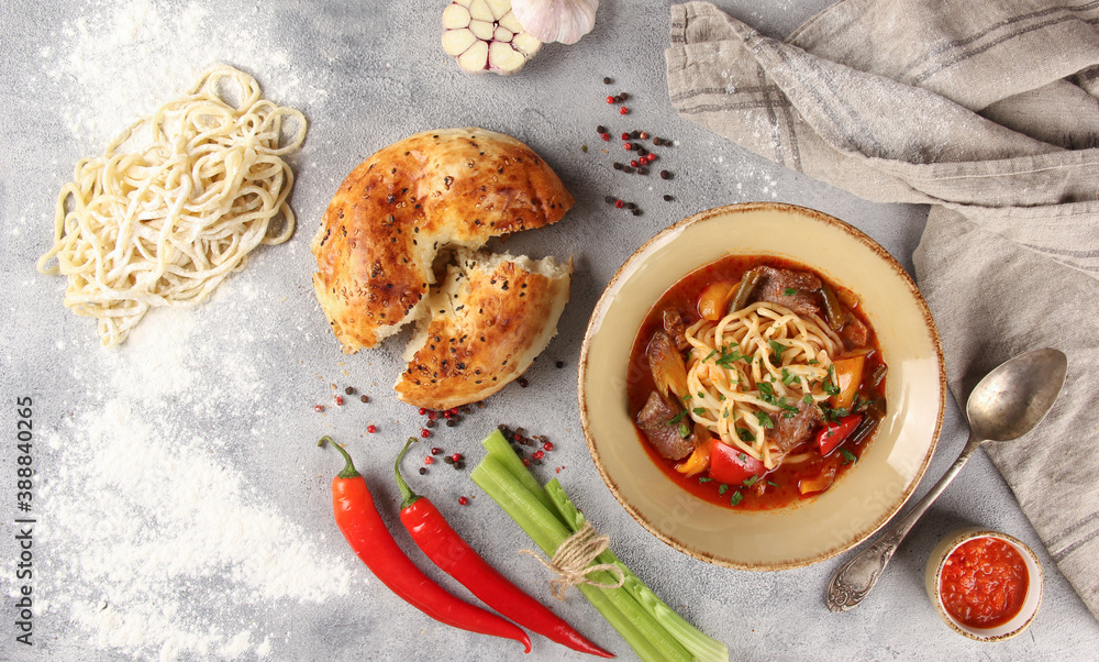 The Eastern cuisine. Uzbek soup. Lagman with lamb, noodles, vegetables,sauce, tandoor bread. Chili pepper, garlic, flour, spoon on gray background. Background image, copy space. Flatlay, top view