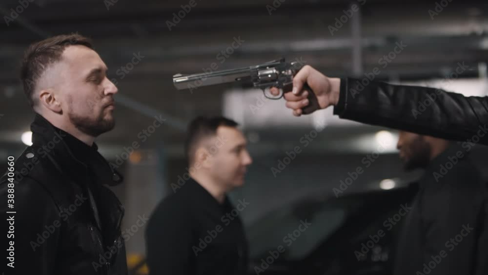 Medium closeup of armed Middle Eastern criminal with tattoo on neck pointing with handgun at forehead of another gangster standing in abandoned underground parking lot Medium closeup of armed Middle Eastern criminal with tattoo on neck pointing with handgun at forehead of another gangster standing in abandoned underground parking lot