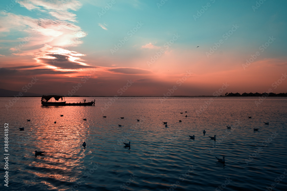 Silhouette of a fishing boat and seagulls on the sea on sunset.