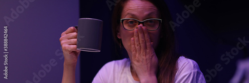 Portrait of tired young woman yawning sitting in room with cup of coffee and accounting money from piggy bank. Saving up for future. Finance and family budget concept photo