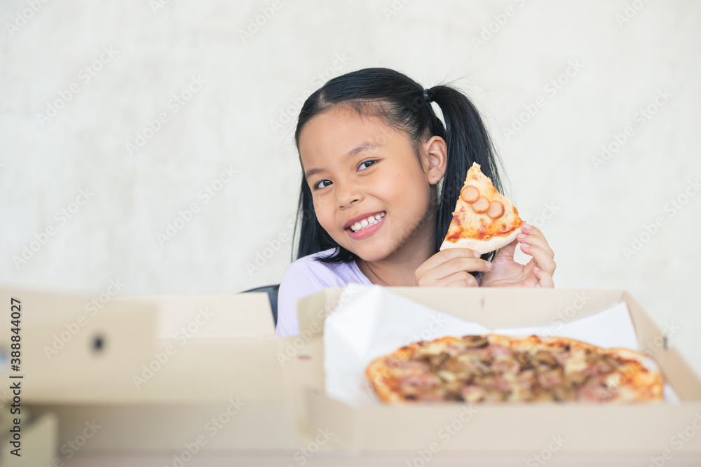 Asian children girl in purple shirt with plaits is enjoy eating a piece of pizza at home. Asian children girl in purple shirt with plaits is enjoy eating a piece of pizza at home.