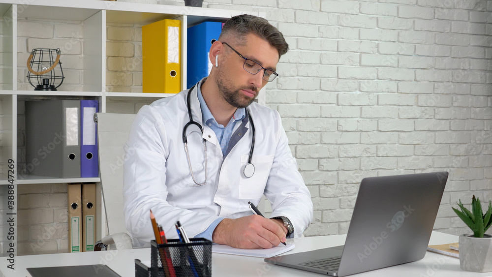 Doctor in medical coat wireless earphones consults patient online video call laptop webcam, writes symptoms in notebook. Man assistant in hospital office listens client uses virtual chat computer app Doctor in medical coat wireless earphones consults patient online video call laptop webcam, writes symptoms in notebook. Man assistant in hospital office listens client uses virtual chat computer app
