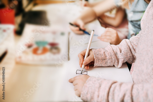 A little girl next to her brother sits at home draws on paper with a felt-tip pen and a pen during studying. Child education at home. Quarantine covid coronavirus concept. Copyspace