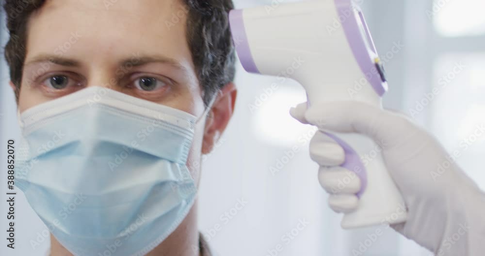 Man wearing face mask getting his temperature measured at office Man wearing face mask getting his temperature measured at office