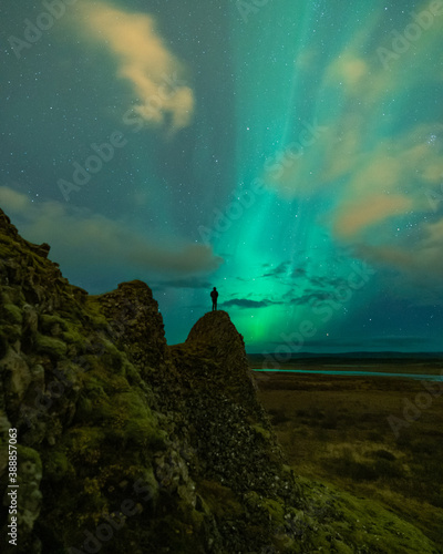 An adventure solo traveler posing with the beautiful northern lights also known as aurora borealis in the background. A breathtaking nature of Iceland as nordic country