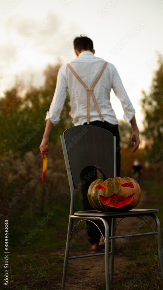 Halloween jack o lantern in front of man with knife - obrazy, fototapety, plakaty 