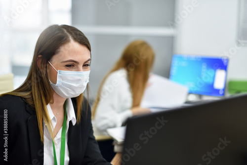 Happy woman office manager in protective mask works at computer in modern office