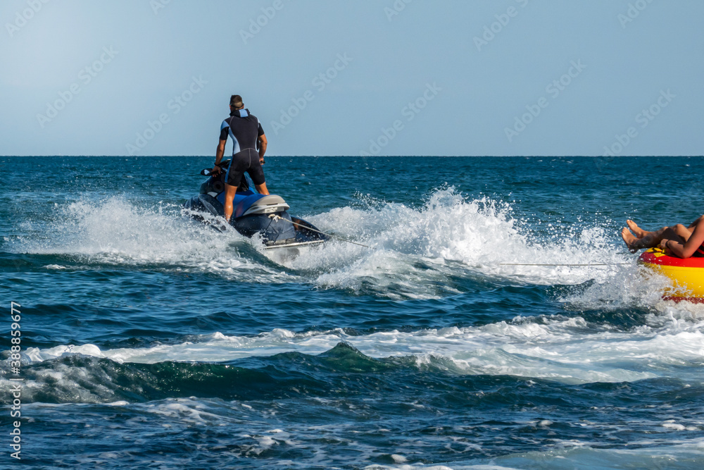 A jet ski at high speed pulls an inflatable boat with a passenger. The passenger image is cut off. Blurred into motion. Defocused image.