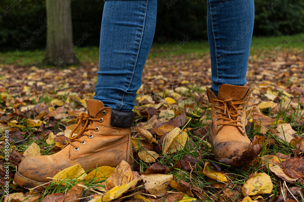 Fototapeta premium Detail picture of two yellow boots on the grass surrounded by leaves that have fallen down from the trees during the autumn season