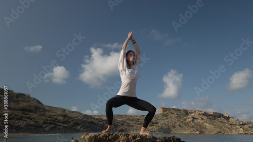 Young caucasian woman brunette doing yoga on rocky beach against blue sky. High quality photo photo