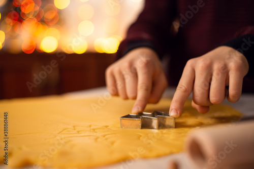 Boy makes shortbread of christmas tree form on the table. Fingers of a child on a dough; festive atmosphere in the kitchen before holidays.