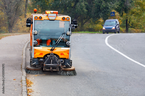 Fototapeta Naklejka Na Ścianę i Meble -  A street sweeper with two front brushes sweeps the street.