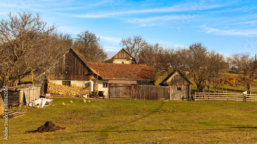 An old plain village with grass in Romania with hut and trees. There is a nice blue sky with clouds. A typical European village.