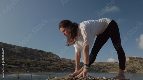 Young caucasian woman brunette doing yoga on rocky beach against blue sky. High quality photo photo