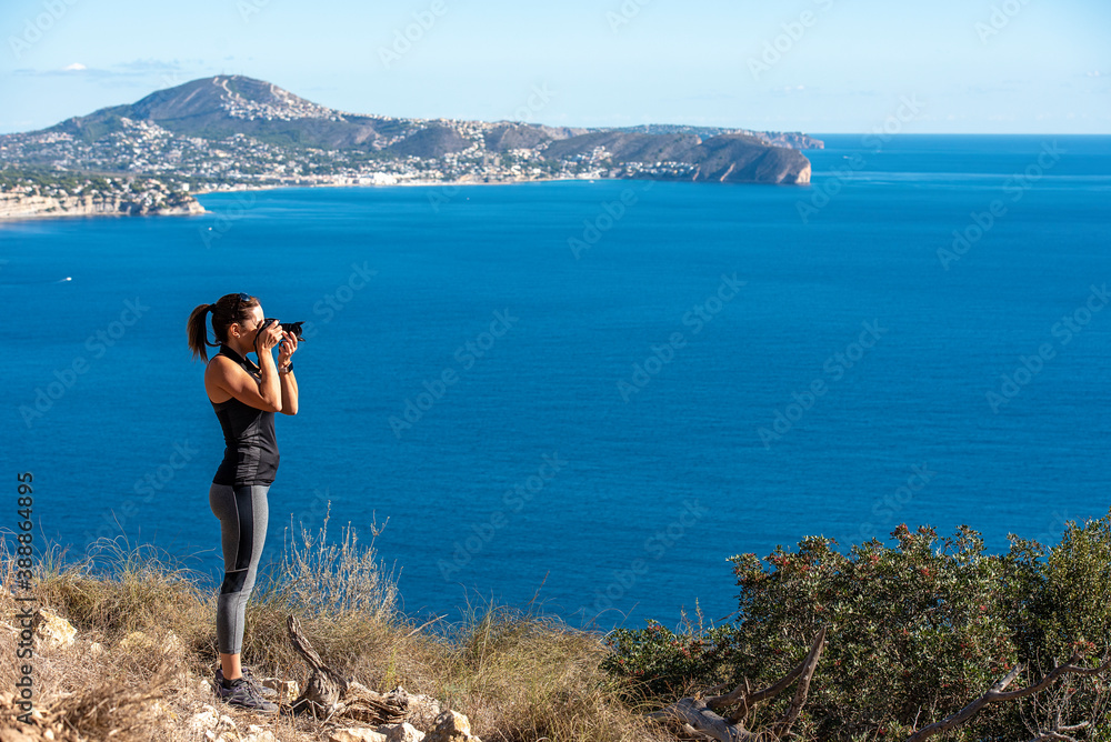 Woman taking pictures with her camera to the landscape, in nature from the Peñon de Ifach in Calpe