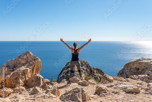 Rear view of a woman having a good time on a trip to the mountains  standing on the edge of the mountain  enjoying her view  with open arms  on a sunny day  - 