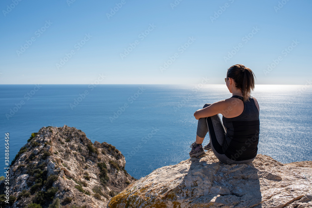 Woman with sportswear sitting on some rocks observing the landscape of the Mediterranean Sea