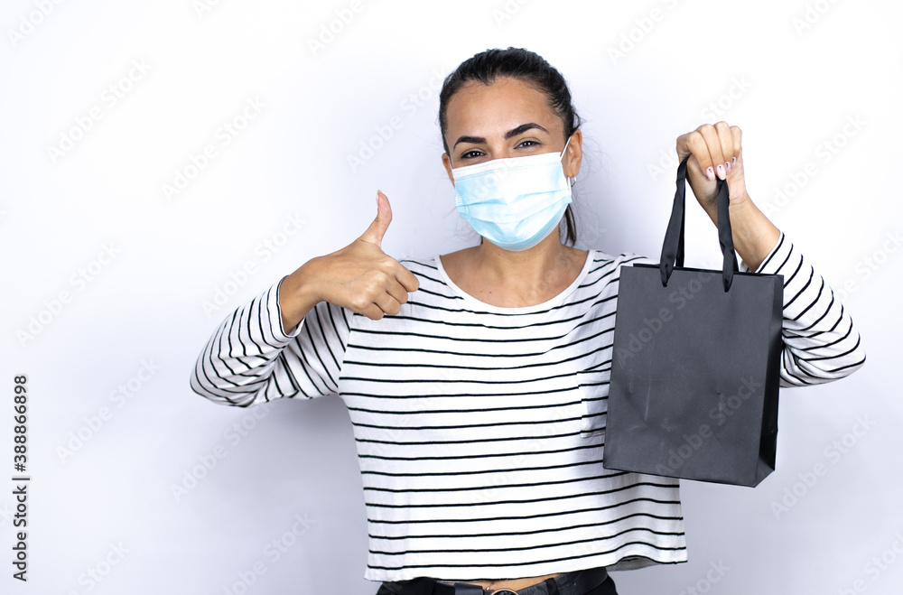 Young beautiful woman holding a black shopping bag wearing a medical mask to protect herself from the coronavirus . Black Friday Young beautiful woman holding a black shopping bag wearing a medical mask to protect herself from the coronavirus . Black Friday